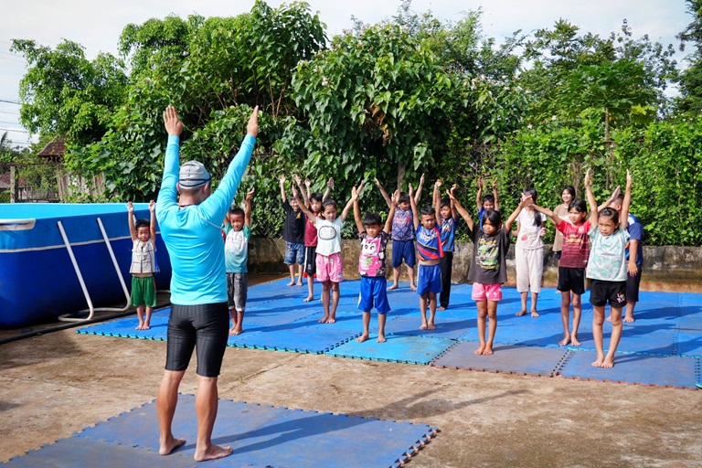 Mai Van Chuyen instructs the children to warm up before the swimming lesson with some stretches outside.